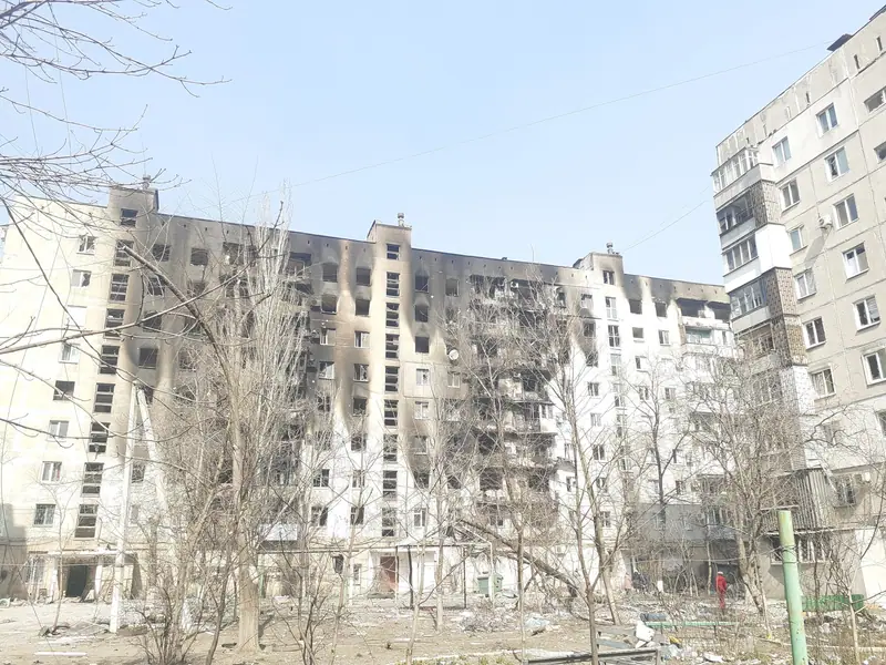 A nine-storey apartment block with fire-blackened facades and burnt-out windows above a courtyard littered with debris