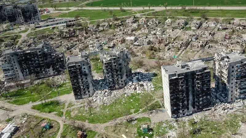 An aerial view of several burnt-out apartment blocks, some partly collapsed with rubble around them, and many ruined houses behind them