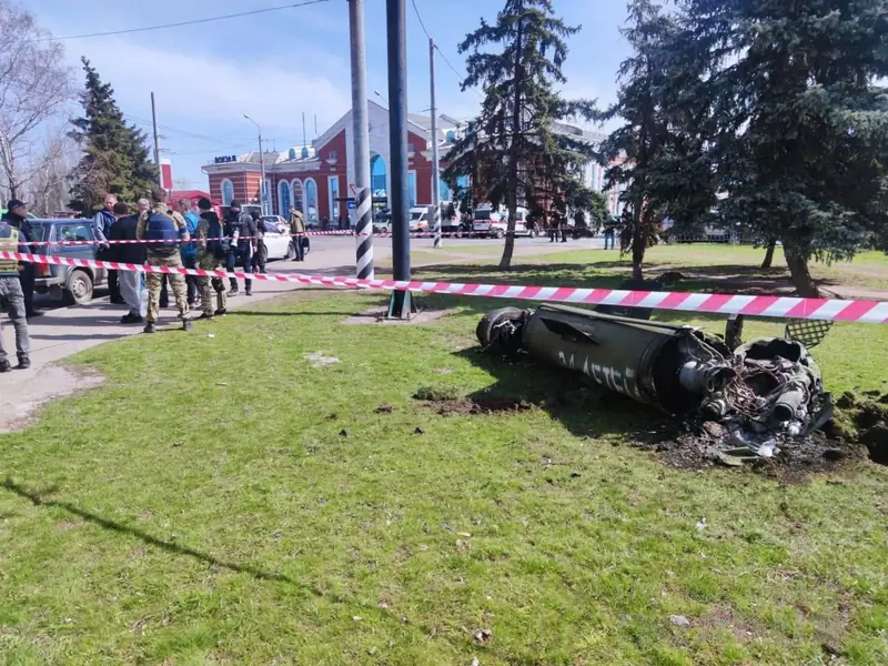 The large tail section of a missile lying on the grass behind a cordon tape in front of Kramatorsk railway station, with police and soldiers standing nearby