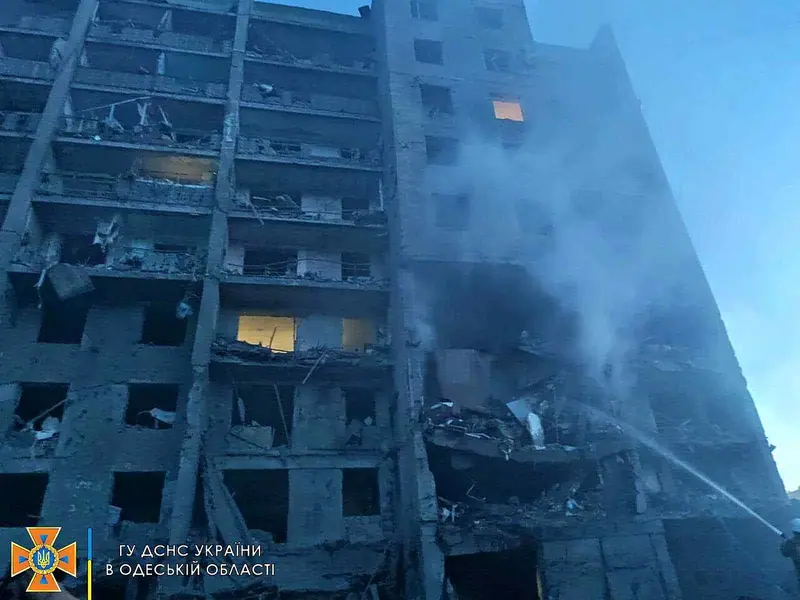A multi-storey apartment building at dawn with its facade torn open and a section collapsed, as firefighters spray water on the smouldering wreckage