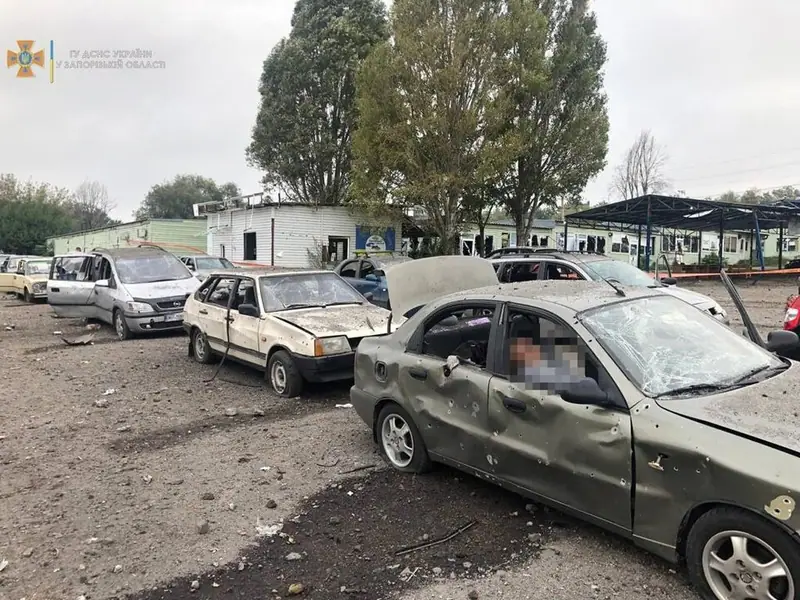 Cars riddled with shrapnel holes and with shattered windows at the strike site. A victim inside one car has been blurred