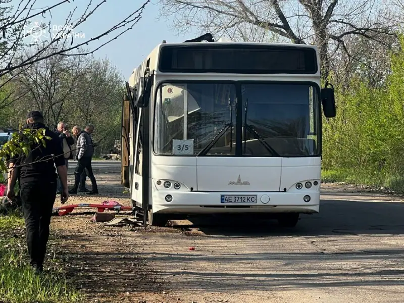 A white city bus parked on a road with its front door open, with people standing nearby and a stretcher on the ground