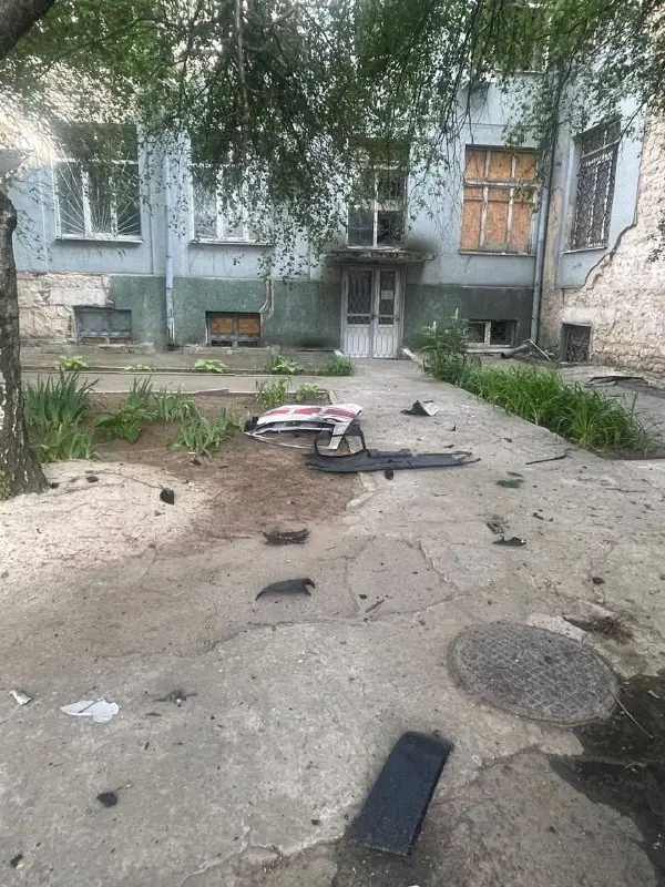 Debris on a concrete yard in front of a hospital building, including pieces of a white and red vehicle panel