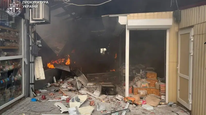 A burning market pavilion with flames, smoke and scattered debris and goods in front of a shop