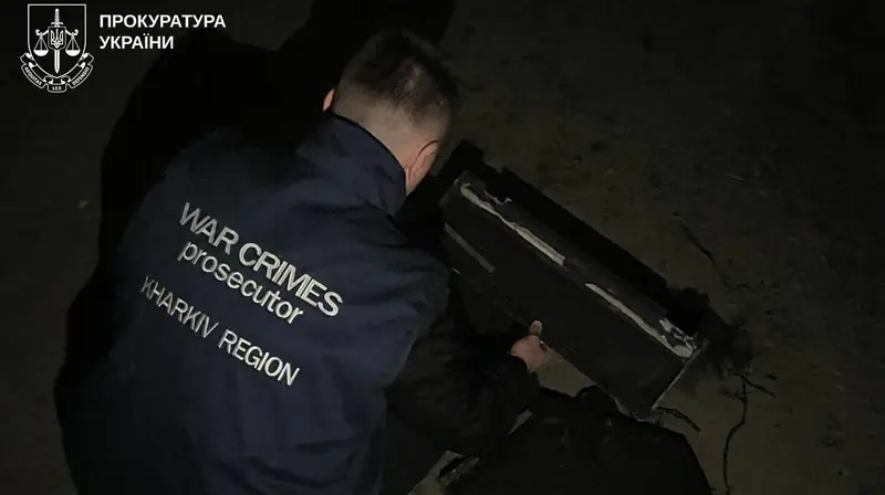 A war crimes prosecutor from Kharkiv region examining a piece of a weapon on the ground at night