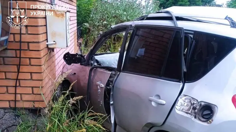 A silver SUV with a damaged, open front door and a torn roof, standing against a brick wall