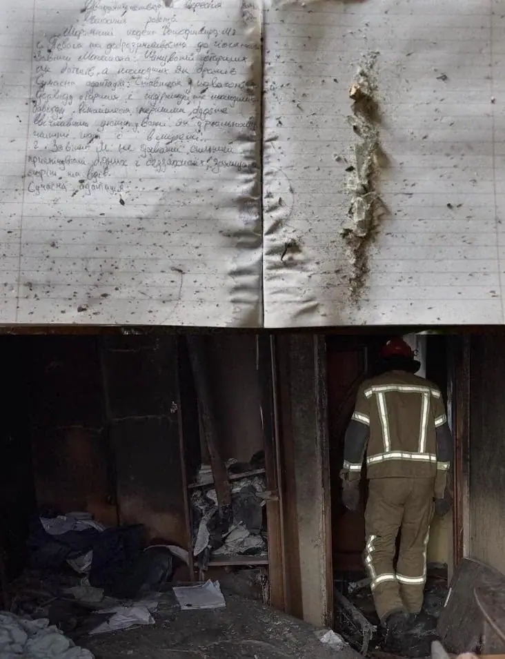 Top: two pages of a handwritten school notebook in Ukrainian, stained and scorched along the centre fold. Bottom: a firefighter in protective gear walking into a burnt-out room.